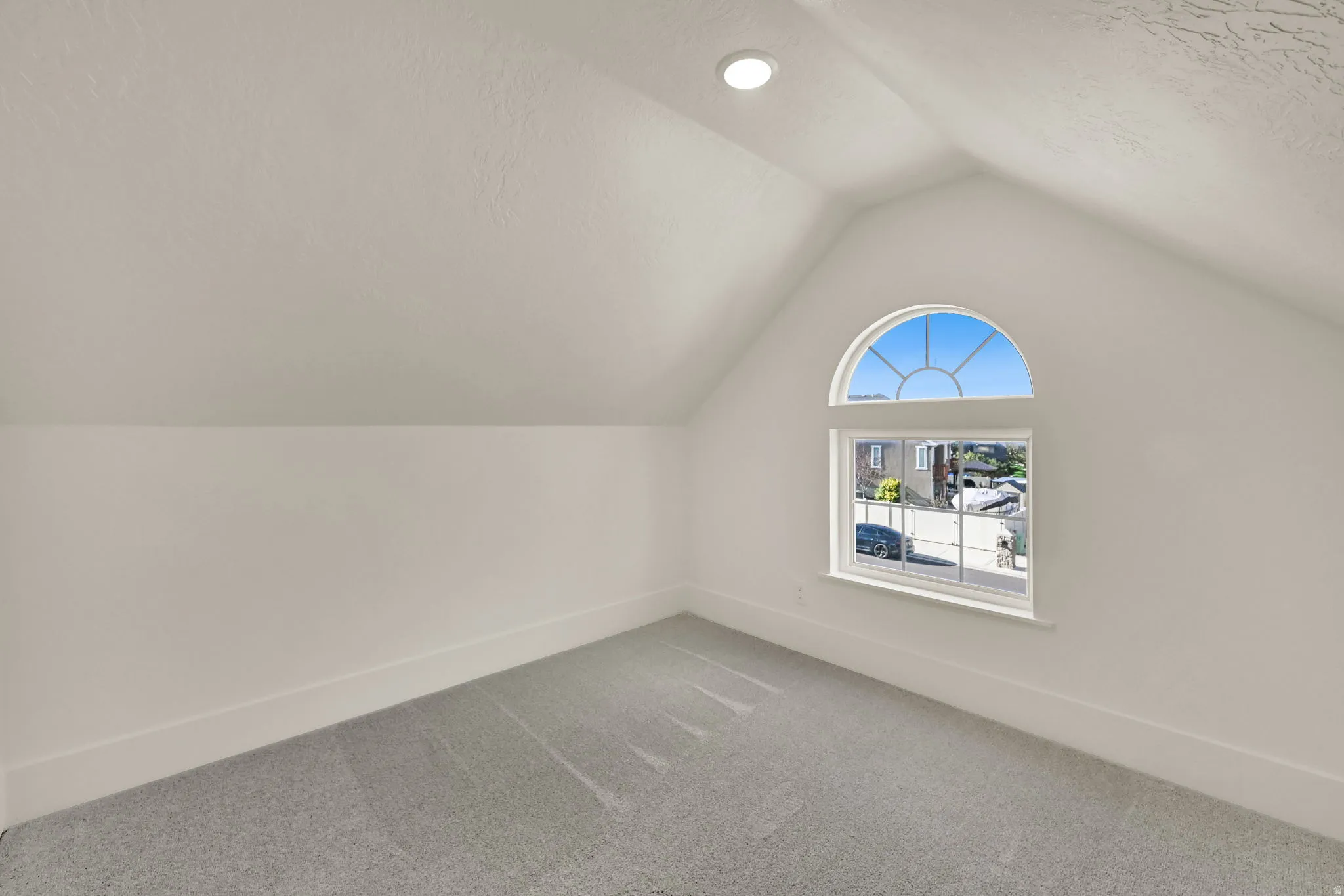 Vaulted ceiling, recessed lighting, arched window with divided lites, light gray carpet, and white painted walls
