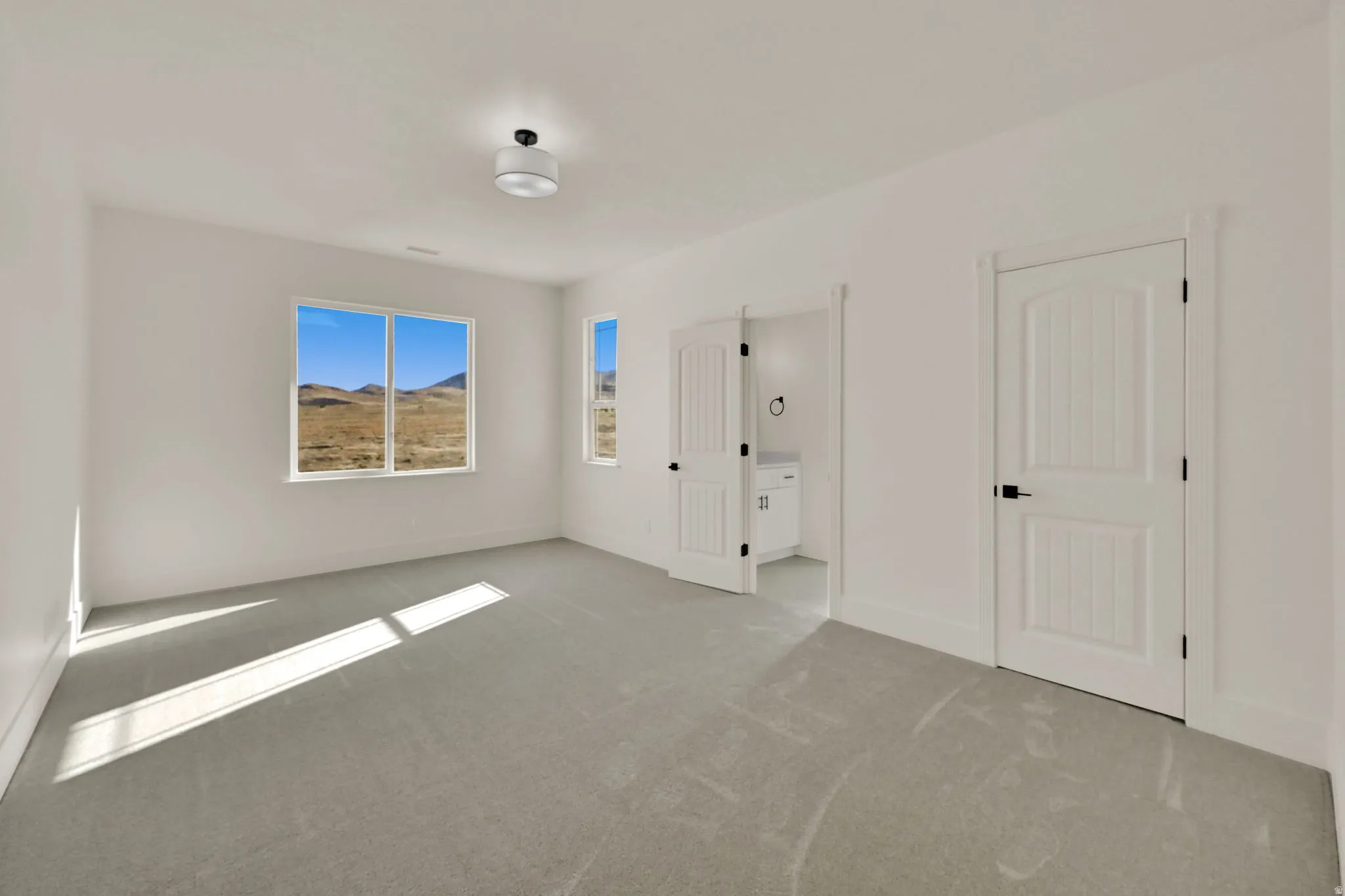 Spacious room featuring light gray carpeting, crisp white walls, multiple windows with a natural landscape backdrop, and white paneled doors with black hardware