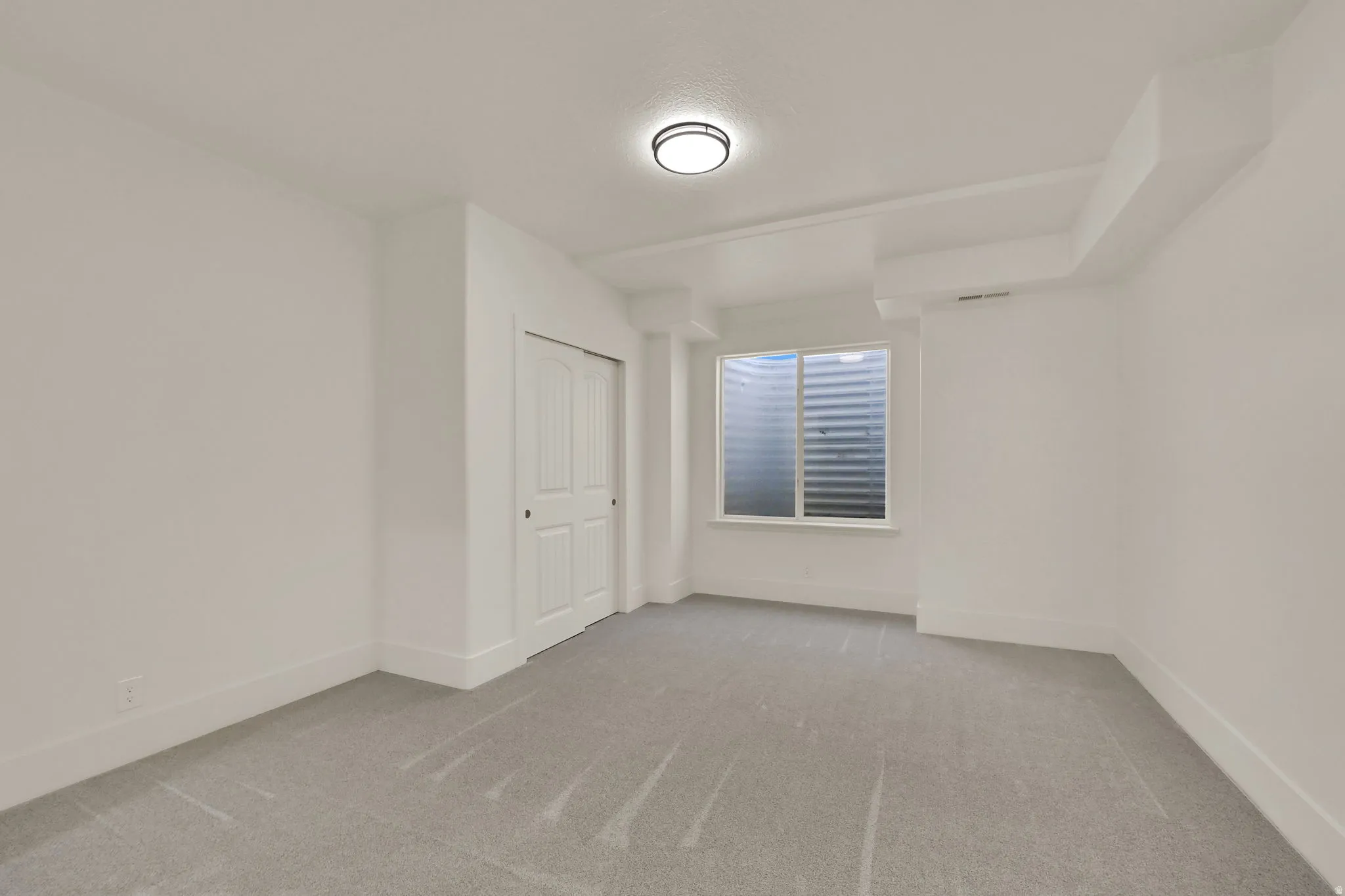 Recessed window with horizontal blinds, flush-mount ceiling light, light-toned carpeting, and bi-fold closet doors