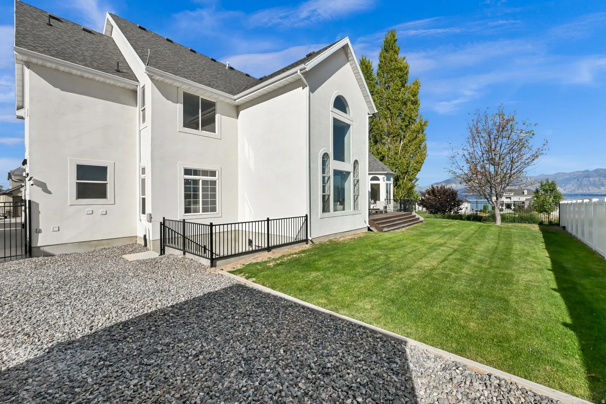 White stucco exterior with a multi-pane arched window and a grey shingled roof
