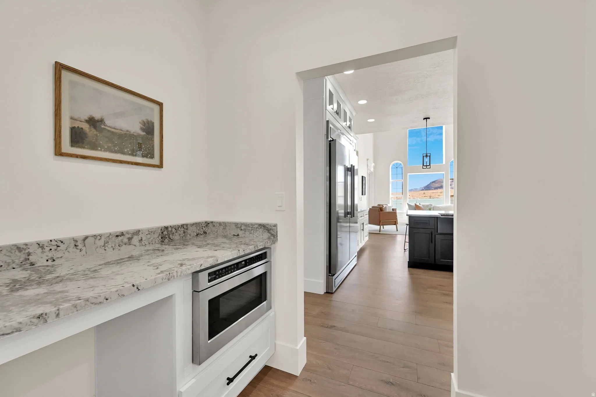Built-in microwave with white cabinetry, granite-style countertop, wood-finish flooring, and arched windows