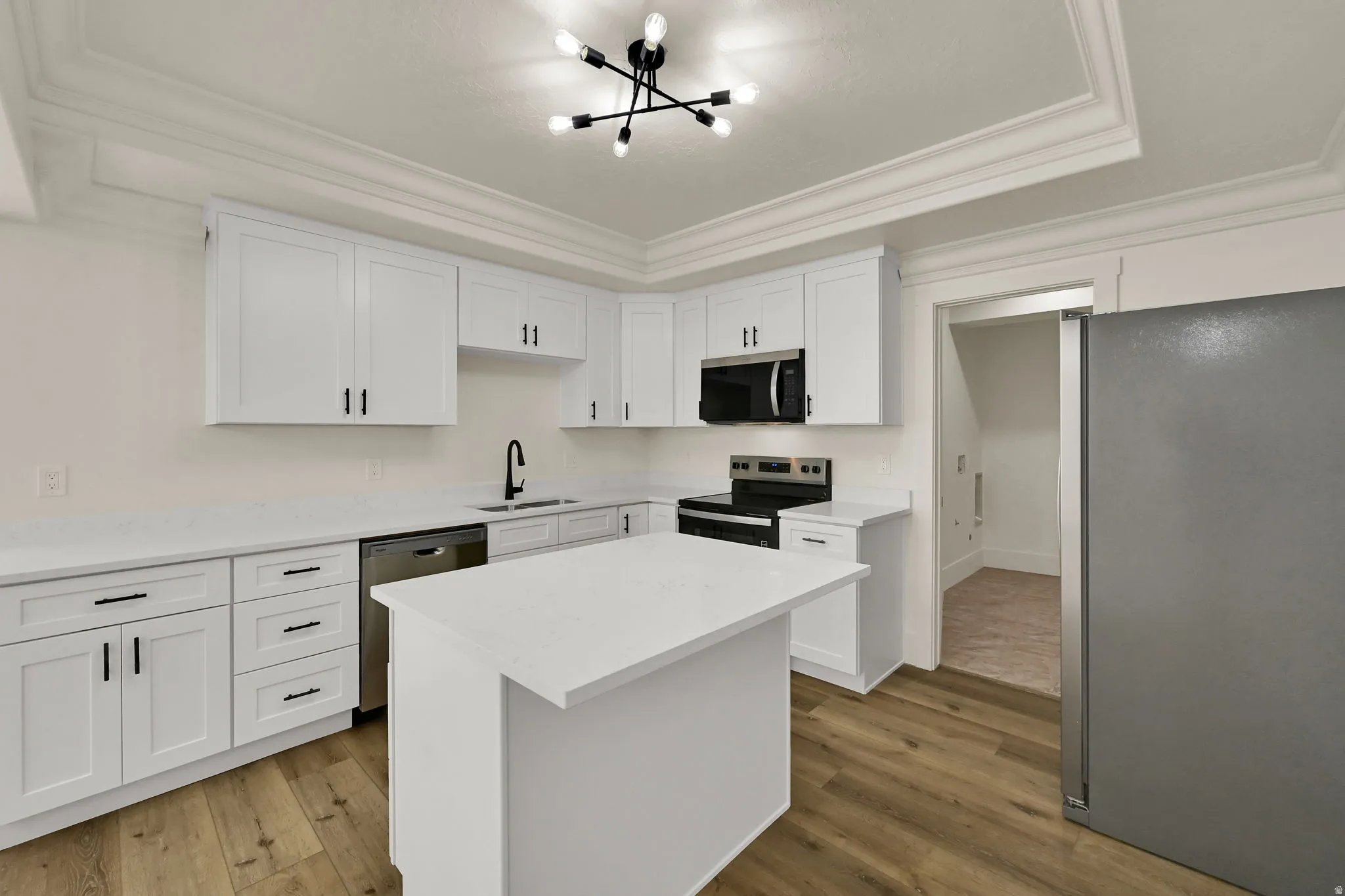 Modern kitchen featuring white shaker cabinetry, stainless steel appliances, a center island, and wood-finish flooring