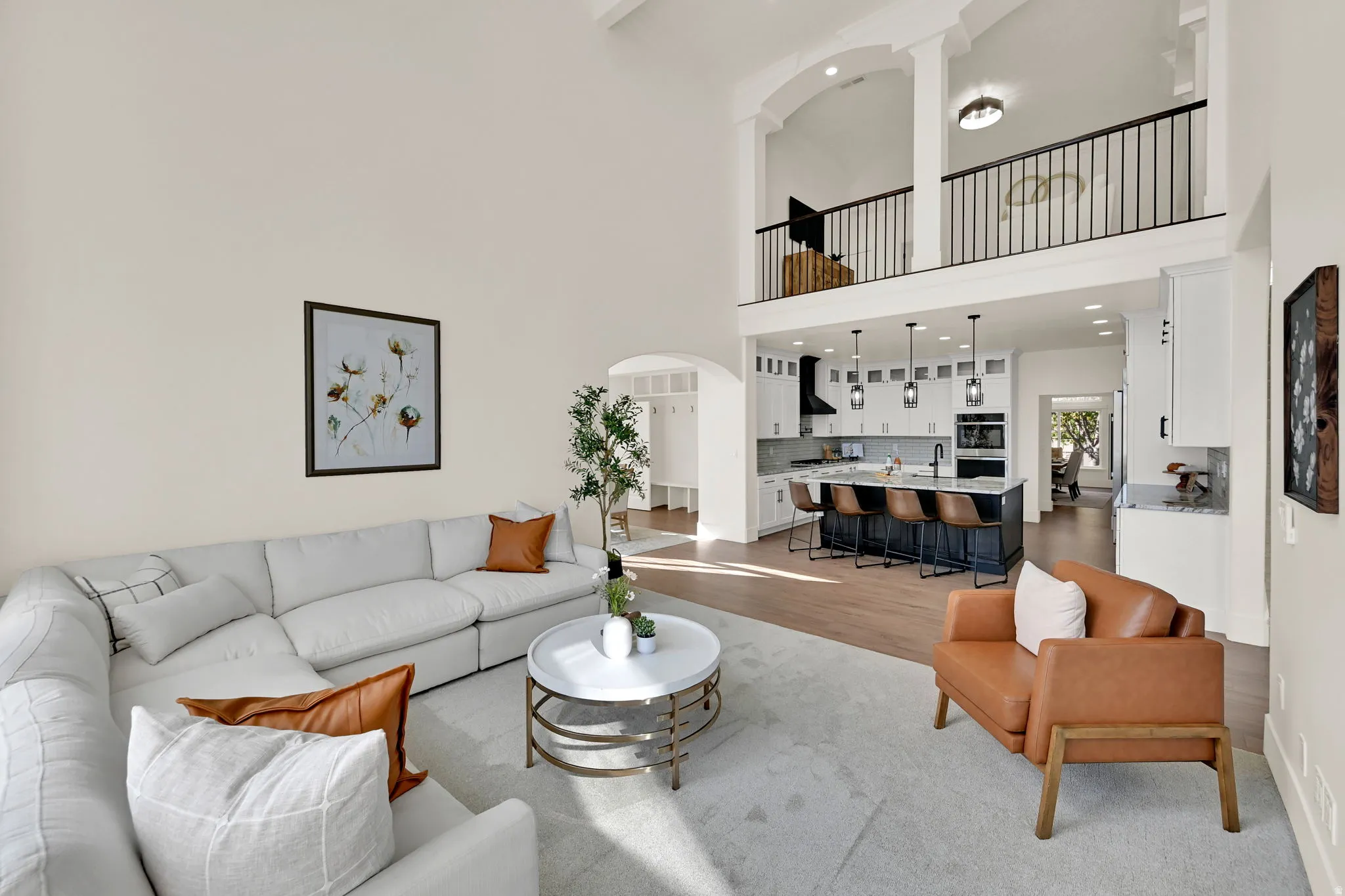 Vaulted ceiling with an open mezzanine, modern kitchen with a large island, wood-finish flooring, and pendant lighting
