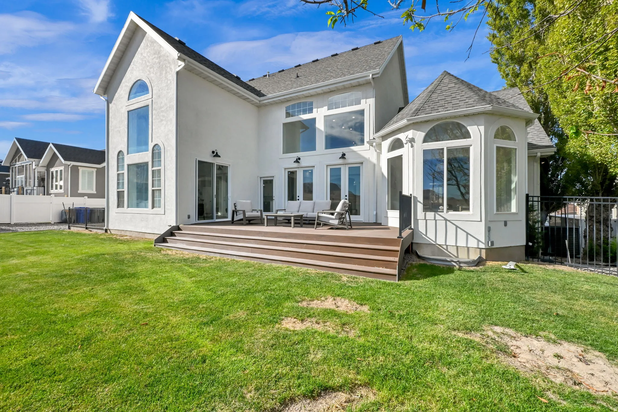White stucco exterior, composite decking, multiple large windows, bay window feature, black metal fencing