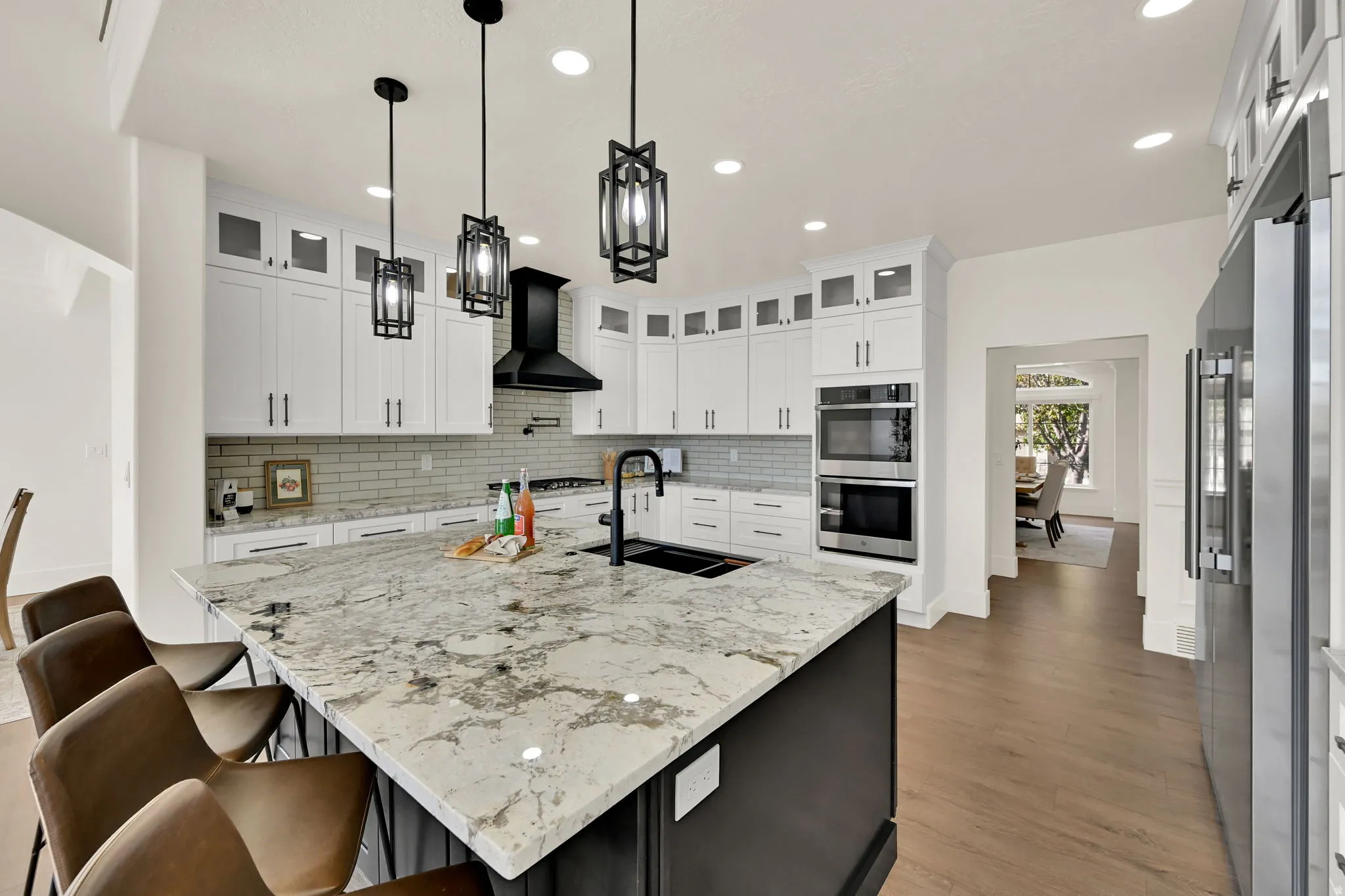 Gourmet kitchen featuring a large island with a stone countertop, built-in stainless steel appliances, white cabinetry, and wood-finish flooring
