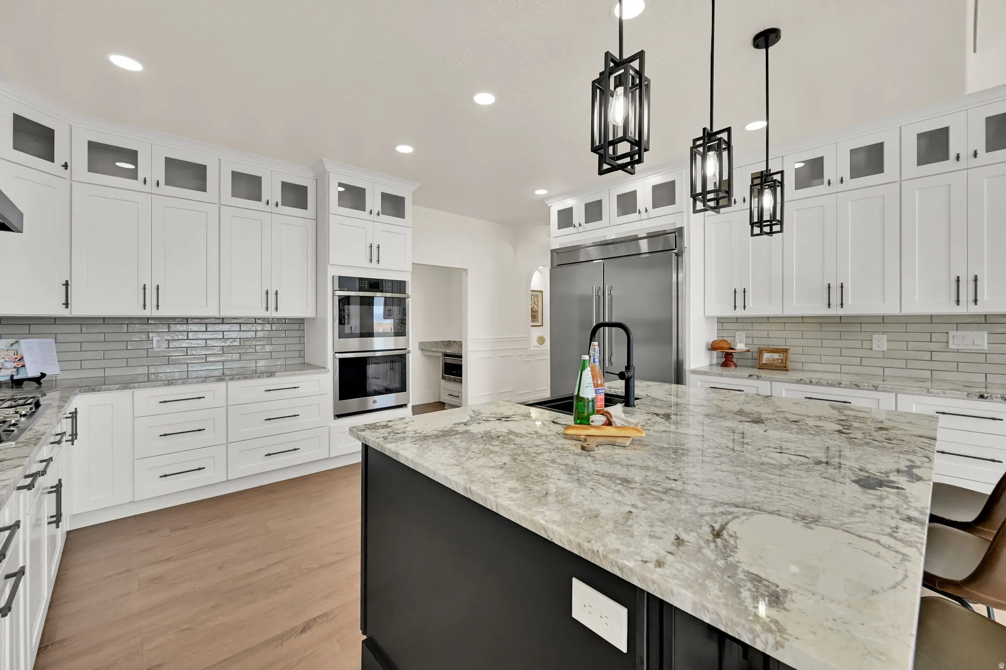Gourmet kitchen featuring white cabinetry, stone countertops, stainless steel appliances, a subway tile backsplash, and wood-finish flooring