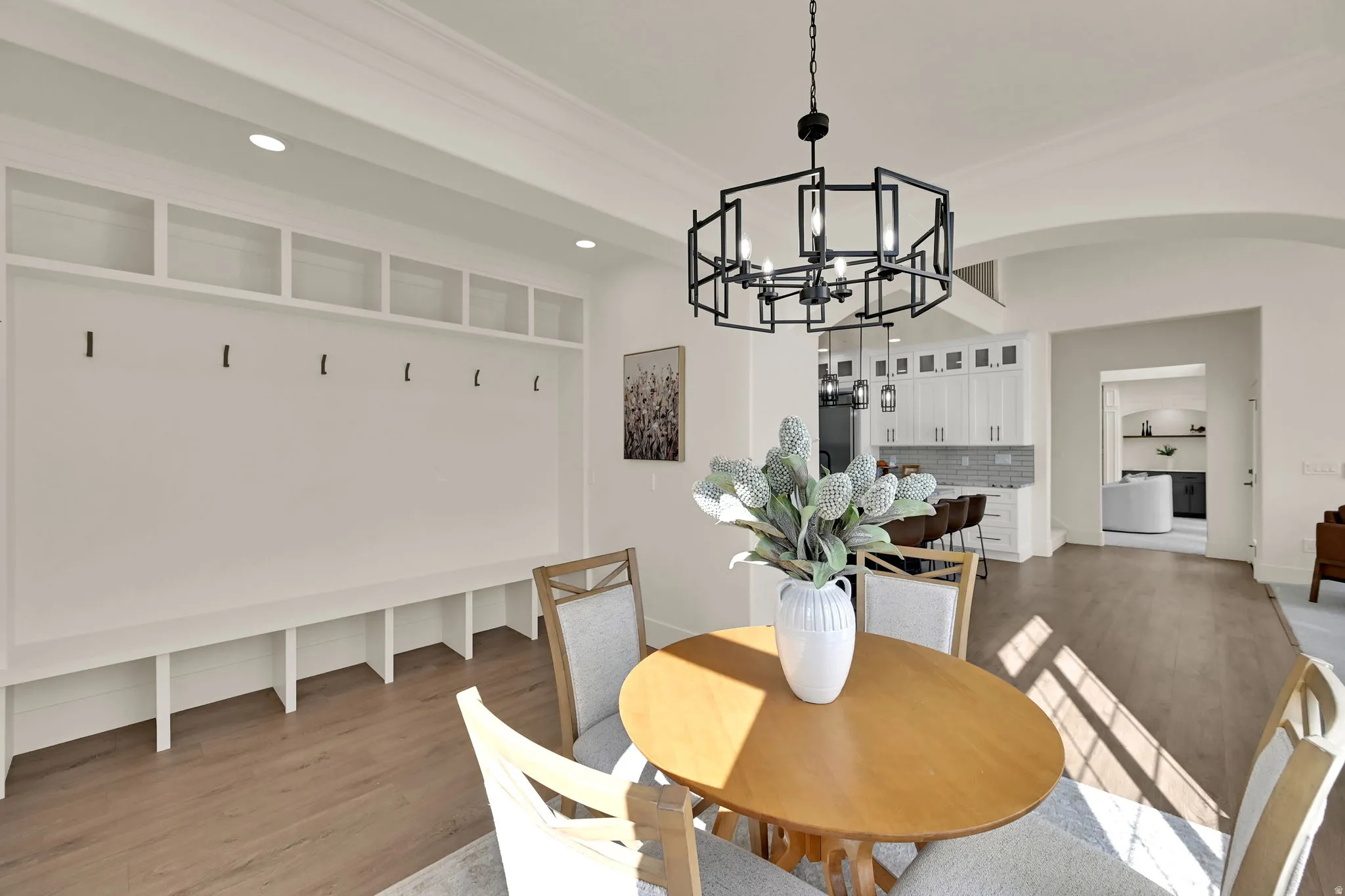 Built-in storage bench with open shelving and coat hooks, wood-finish flooring, recessed lighting, and a contemporary black chandelier