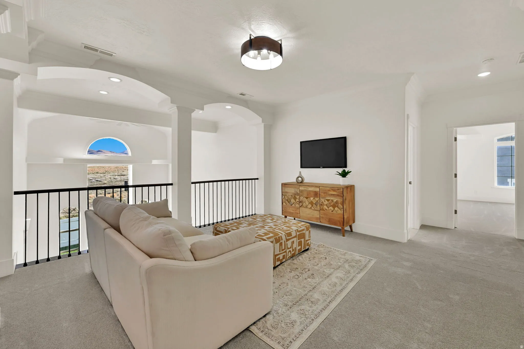 Carpeted loft space with a black metal railing, arched architectural details, and recessed lighting
