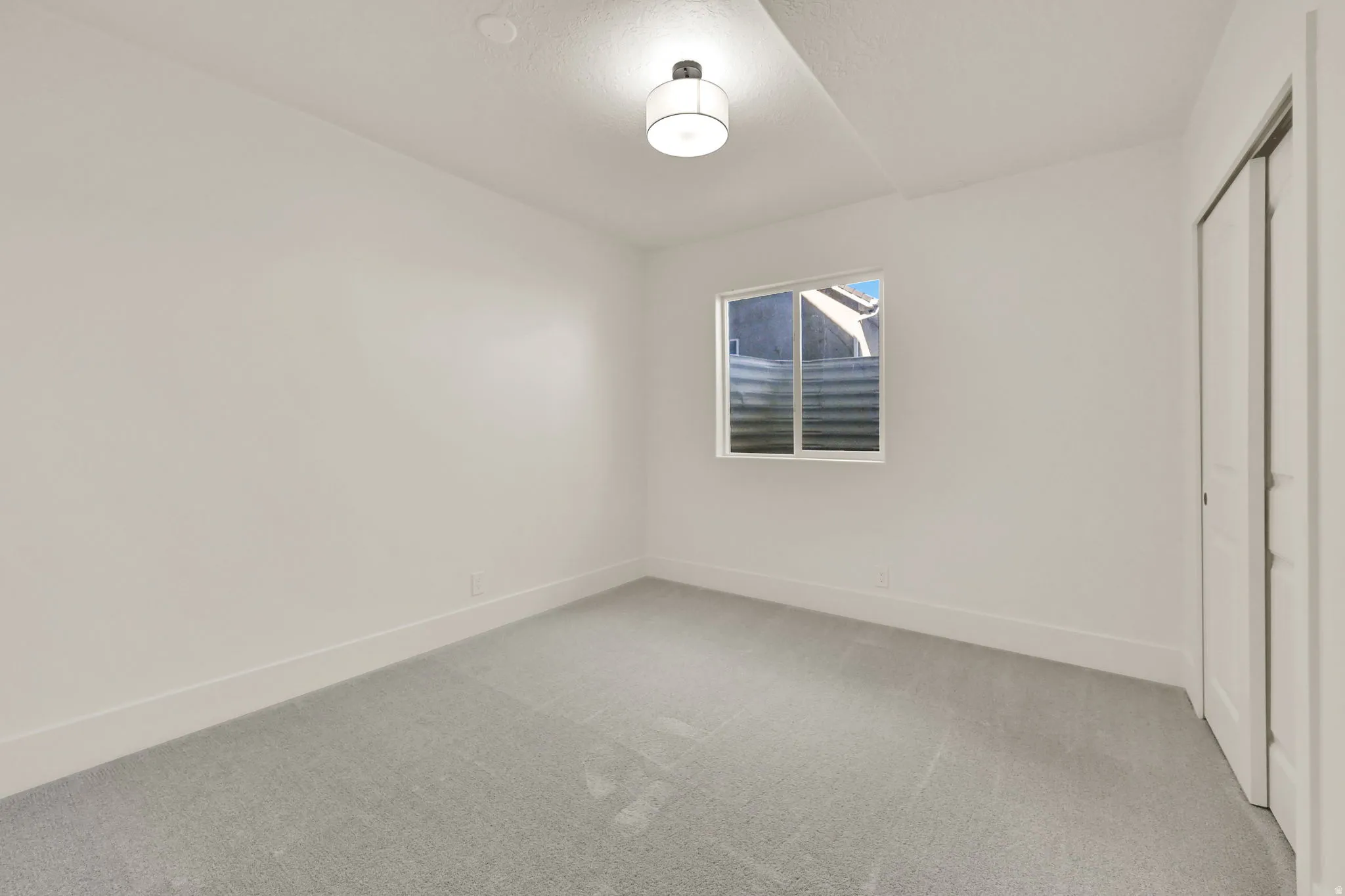 Light gray carpeting, a window with horizontal blinds, and a flush-mount ceiling light fixture