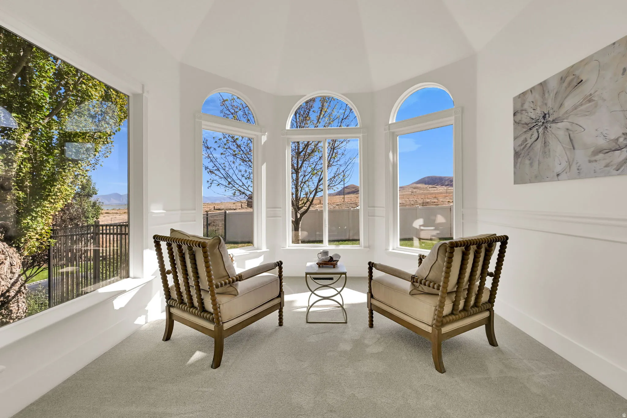 Primary Suite Sun Room with rounded ceiling feature, multiple arched windows, expansive bay window, light-toned carpet, and white wall paneling