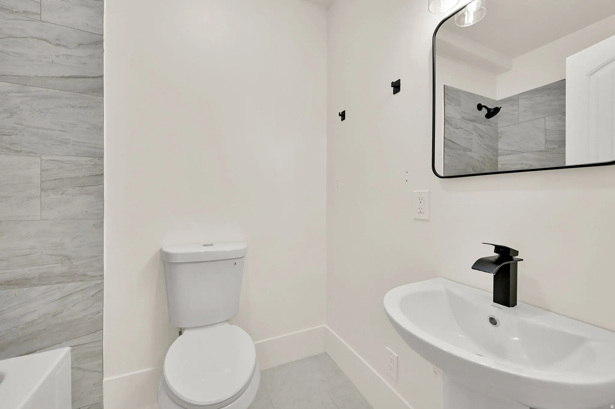 Pedestal sink with a matte black faucet, rectangular framed mirror, and contemporary vanity lighting
