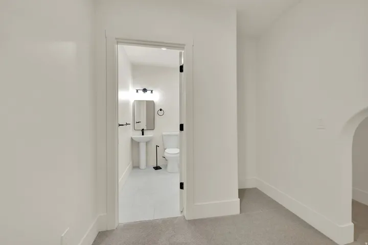 White pedestal sink, modern wall-mounted light fixture, rectangular mirror, toilet, and light-toned flooring