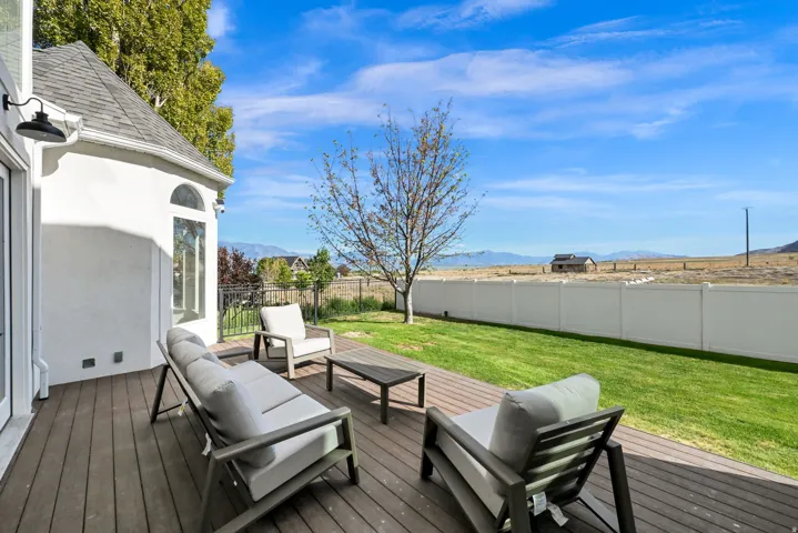 Expansive wood-finish deck, manicured lawn, white privacy fence, arched window, and exterior lighting fixture