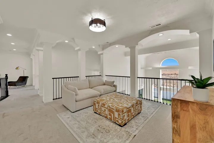 Open-concept upper level featuring white walls, archways, and black metal railings