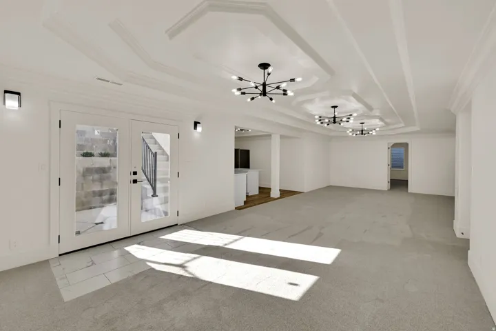 Recessed tray ceilings with contemporary light fixtures, double French doors with transom windows, wall-mounted sconces, and mixed flooring with carpet and tile