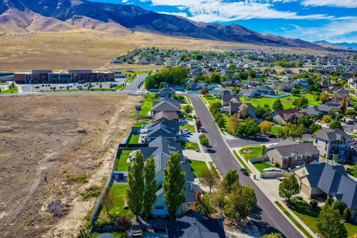 Residential neighborhood with established streets and mature landscaping, bordered by undeveloped land and a distant commercial building, all set against a mountainous backdrop