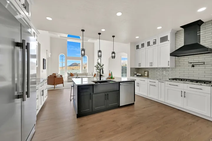 Kitchen featuring wood-finish flooring, white cabinetry, a dark gray island with a sink, stainless steel appliances, and a tiled backsplash