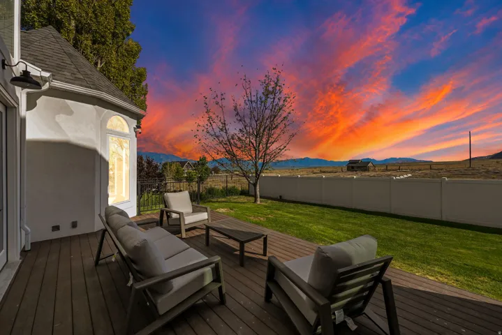 Expansive wood-finish deck with a manicured lawn, a white privacy fence, and an exterior wall featuring a round-top window