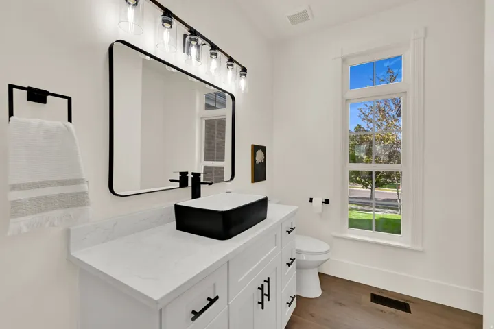 White vanity with a rectangular black vessel sink, black wall-mounted faucet, and a large framed mirror with overhead lighting