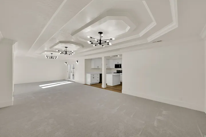 Recessed hexagonal ceiling details, contemporary black chandeliers, light-toned carpeting, white cabinetry, and wood-finish flooring