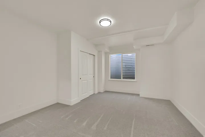 Recessed window with horizontal blinds, flush-mount ceiling light, light-toned carpeting, and bi-fold closet doors