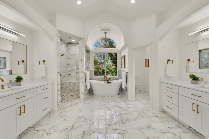 Primary Suite Luxury Bathroom with dual vanity sinks with white cabinetry and gold-tone hardware