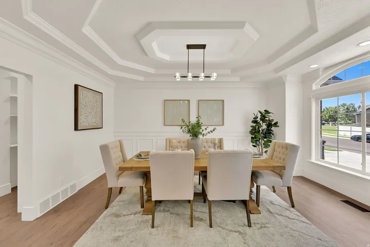 Tray ceiling with crown molding, chandelier, wood-finish flooring, wainscoting, and an arched window