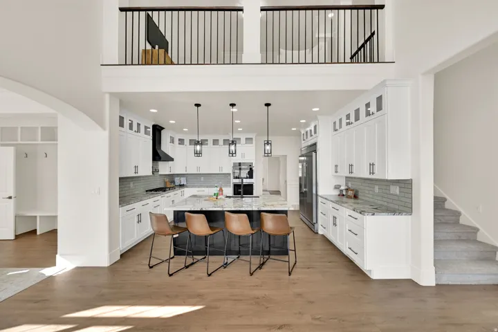 Vaulted ceiling with an upper-level balcony, wood-finish flooring, white cabinetry with dark hardware, kitchen island with granite countertop, and stainless steel appliances
