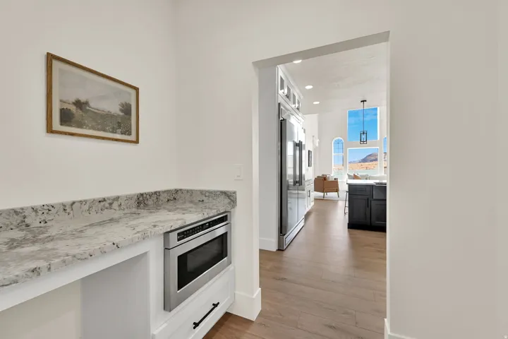 Built-in microwave with white cabinetry, granite-style countertop, wood-finish flooring, and arched windows