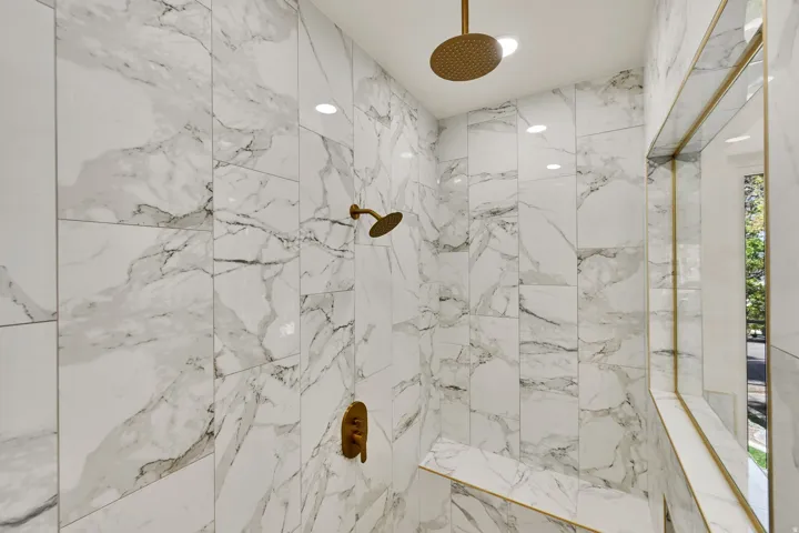 Primary Suite with walk in shower with full-height marble-look tile, rain shower head, hand-held shower, built-in bench, and recessed lighting