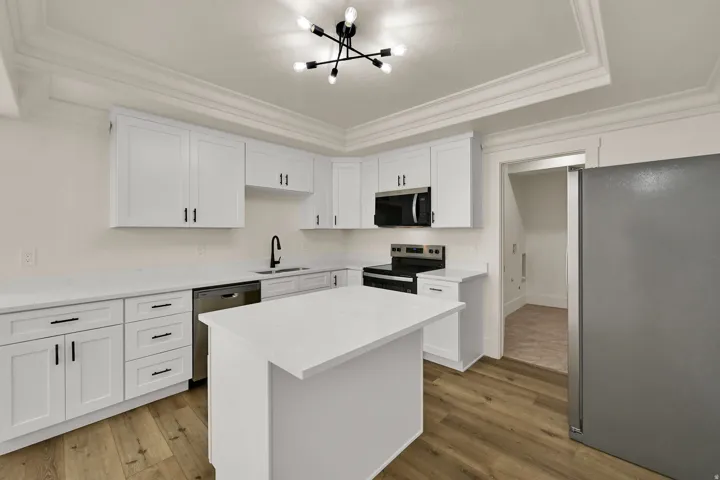Modern kitchen featuring white shaker cabinetry, stainless steel appliances, a center island, and wood-finish flooring