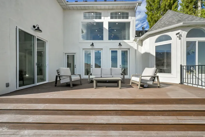 Expansive outdoor deck with multiple entry points, a sliding glass door, double French doors, and large arched windows