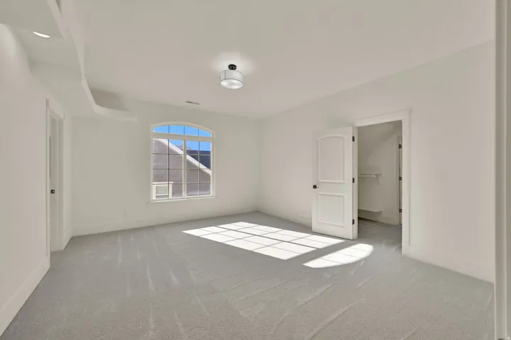 Room featuring light-toned carpeting, an arched window with grid panes, a semi-flush mount ceiling light, and a white paneled door