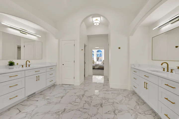 Primary Suite with dual vanities with white cabinetry and gold-finish hardware