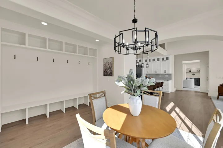 Built-in storage bench with open shelving and coat hooks, wood-finish flooring, recessed lighting, and a contemporary black chandelier