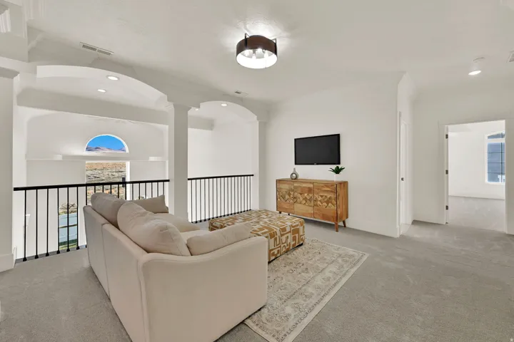 Carpeted loft space with a black metal railing, arched architectural details, and recessed lighting