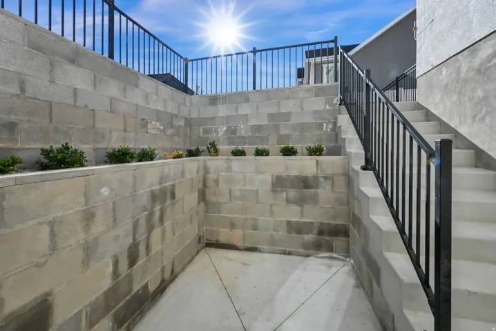 Tiered concrete block retaining walls with integrated planters, concrete steps, and black metal railings