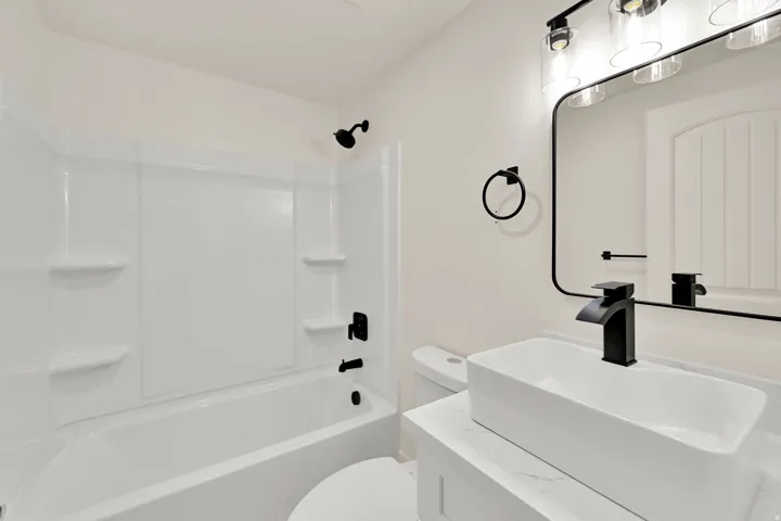 White rectangular vessel sink with a matte black waterfall faucet, framed by a rectangular mirror with integrated lighting