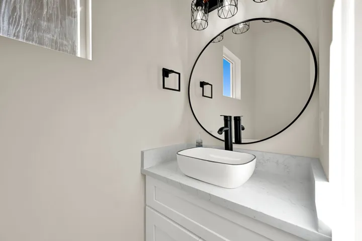 White vanity with shaker-style cabinetry, a light-toned countertop, a vessel sink, and a wall-mounted matte black faucet