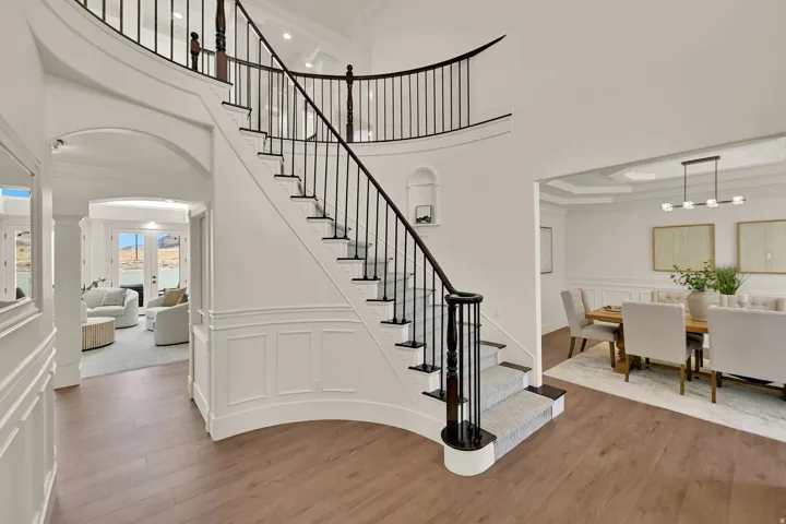 Curved staircase with black wrought iron balusters, wood-finish flooring, wainscoting details, recessed ceiling lighting, and a coffered dining room ceiling