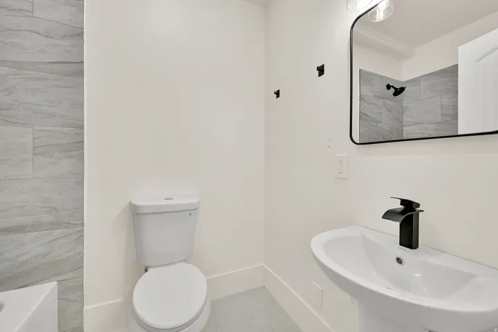 Pedestal sink with a matte black faucet, rectangular framed mirror, and contemporary vanity lighting