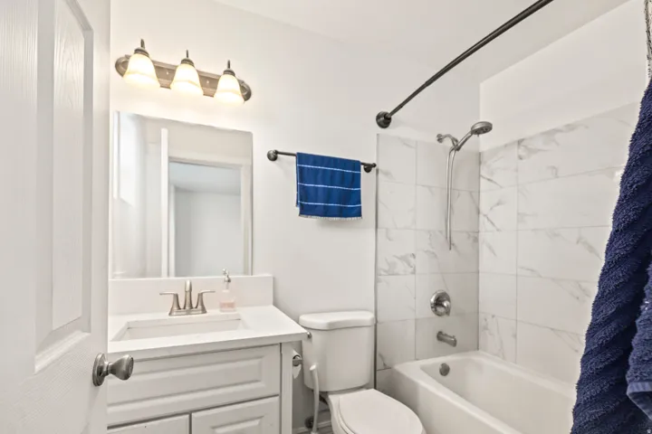 Vanity with integrated sink and chrome faucet, wall-mounted mirror, three-light vanity fixture, white subway tile shower surround, and white bathtub