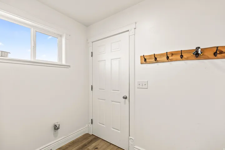 White paneled door with a silver knob, wood-finish flooring, and a window with white trim