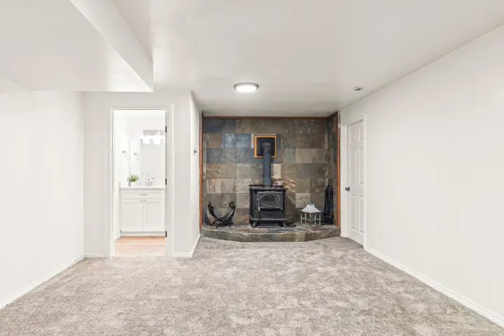Carpeted room featuring a stone-clad wall with a wood-burning stove and a stone hearth