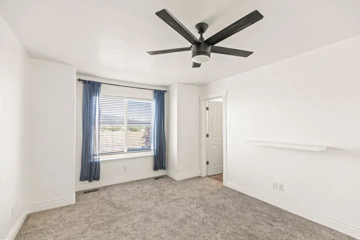 Carpeted room with a ceiling fan, window with blinds, and a wall-mounted shelf