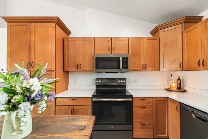 Kitchen featuring wood cabinetry, stainless steel microwave, black electric range, and white countertops