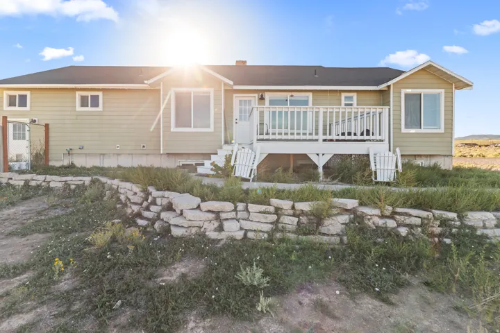 Ranch-style exterior with light green siding, white trim, a rear deck with white railings, and a stone retaining wall