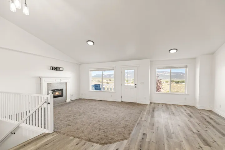 Vaulted ceilings, a built-in fireplace with a white mantel, wood-finish flooring, and a white railing with black newel posts