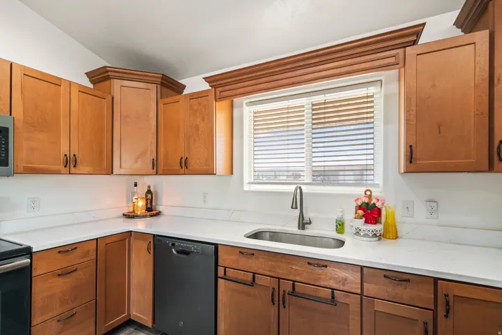 Warm wood cabinetry with dark hardware, white countertops, stainless steel sink with gooseneck faucet, and a black built-in dishwasher