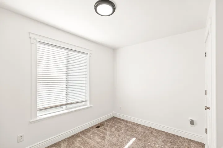 Neutral wall paint, plush carpet flooring, a window with horizontal blinds, decorative window trim, and a flush-mount ceiling light fixture